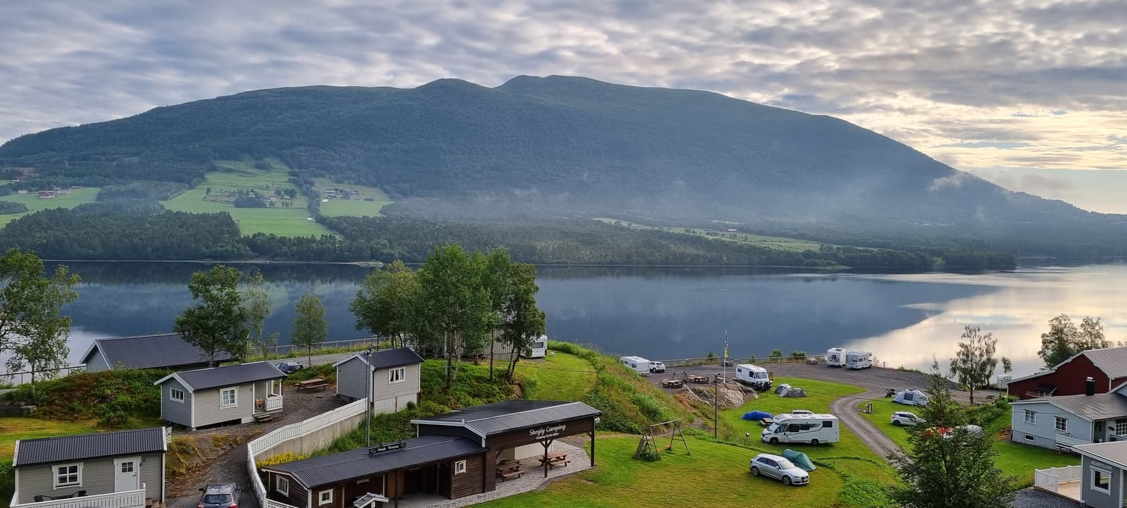 Blick über Campingplatz und See an einem Morgen mit Bodennebel