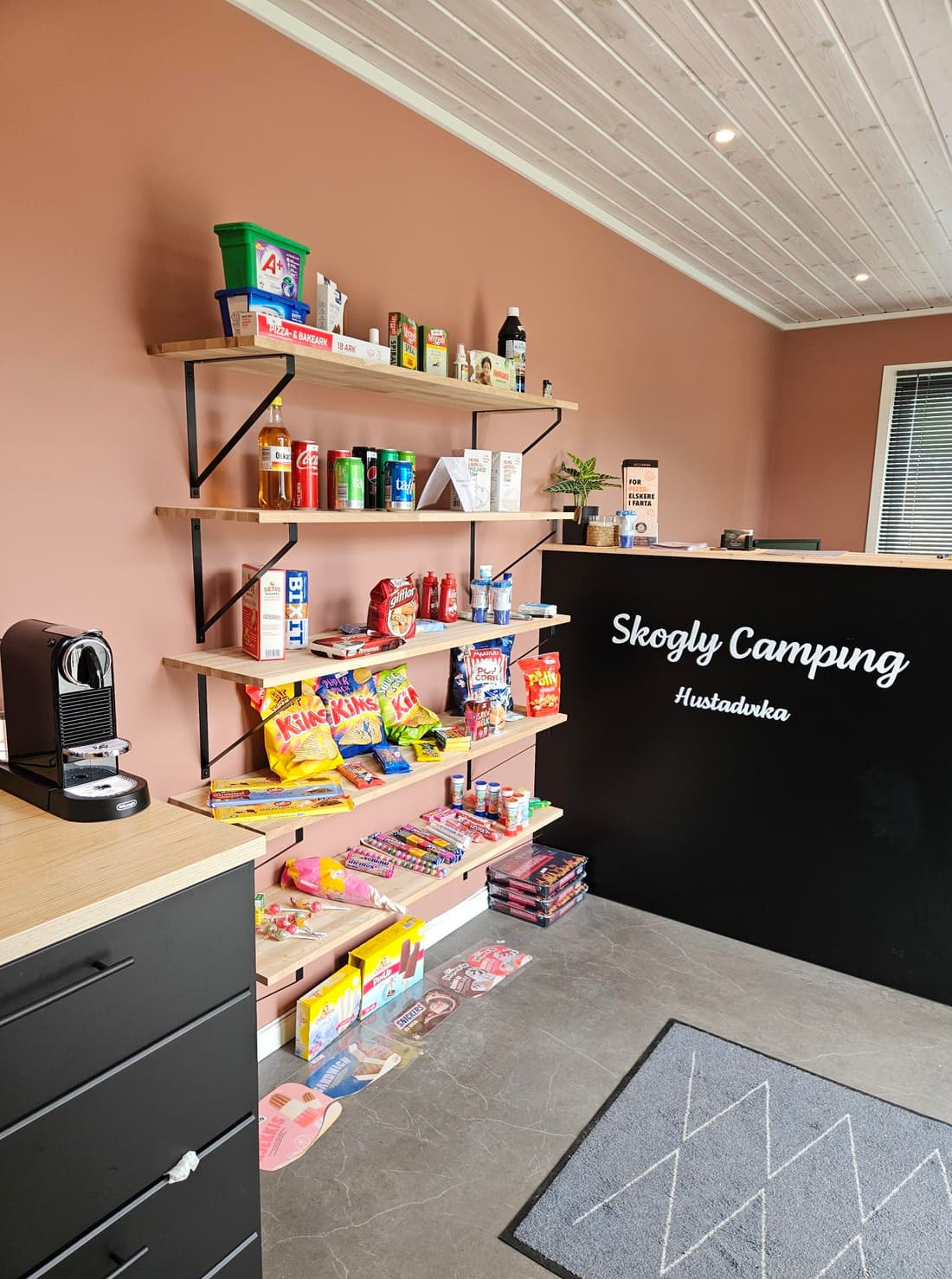 Resepsjonen med kioskhyller, kaffemaskin og disk merket Skogly Camping