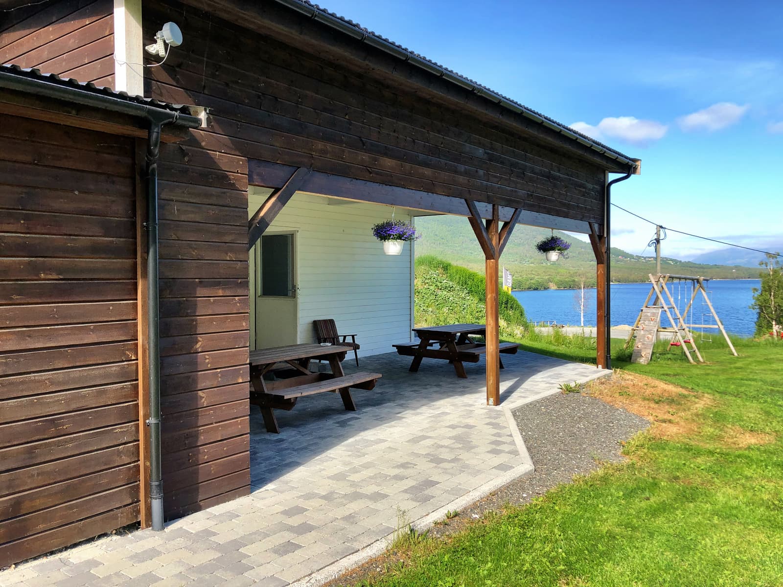 Überdachter Sitzplatz mit Tischen und Bänken, Schaukel und See dahinter