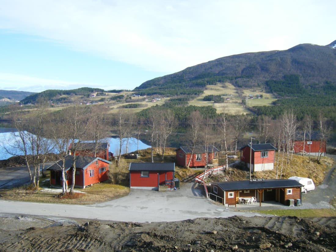Campingplassen sett fra fjellsida, med hytter og vatnet nedenfor