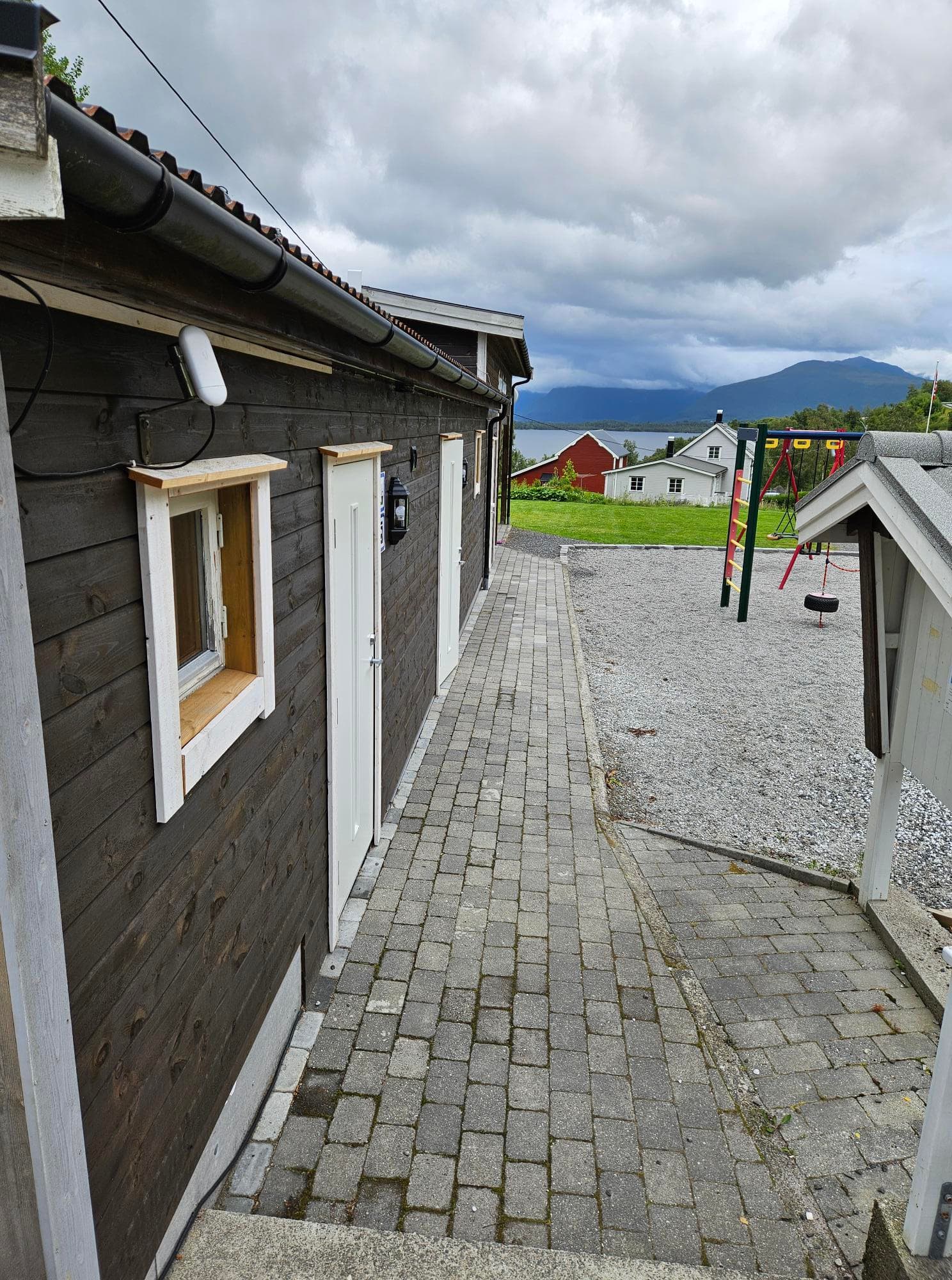 Servicebygget med brostein foran og lekeplassen ved siden av